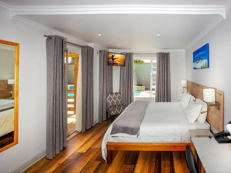 Chambre lumineuse avec un grand lit et un accès à une piscine.