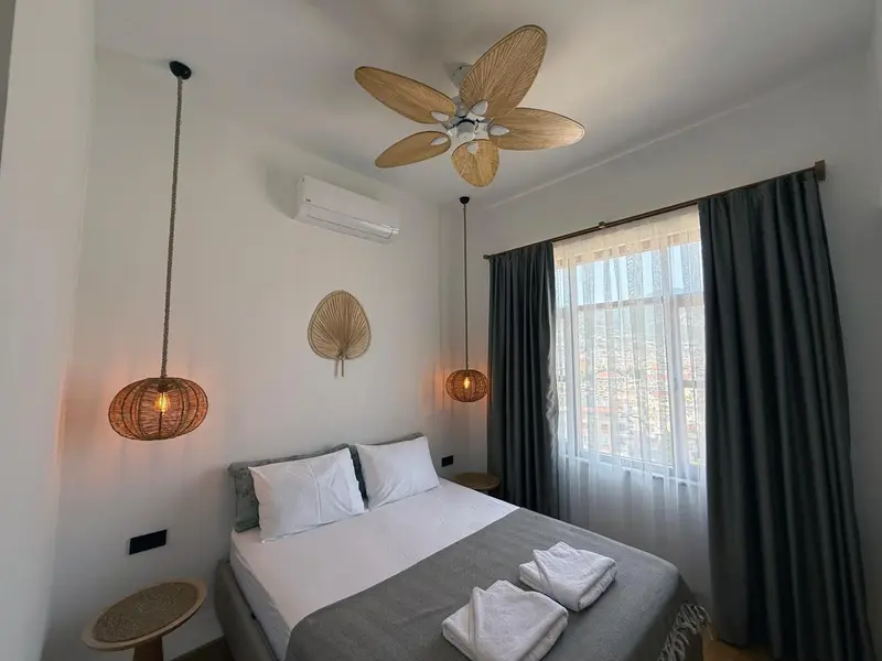 Une chambre lumineuse avec un lit recouvert d'une courtepointe grise et des suspensions en rotin.