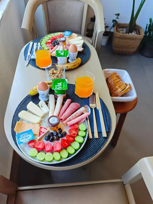 Une table est dressée avec un copieux petit-déjeuner composé de fruits, de viennoiseries et de charcuterie.