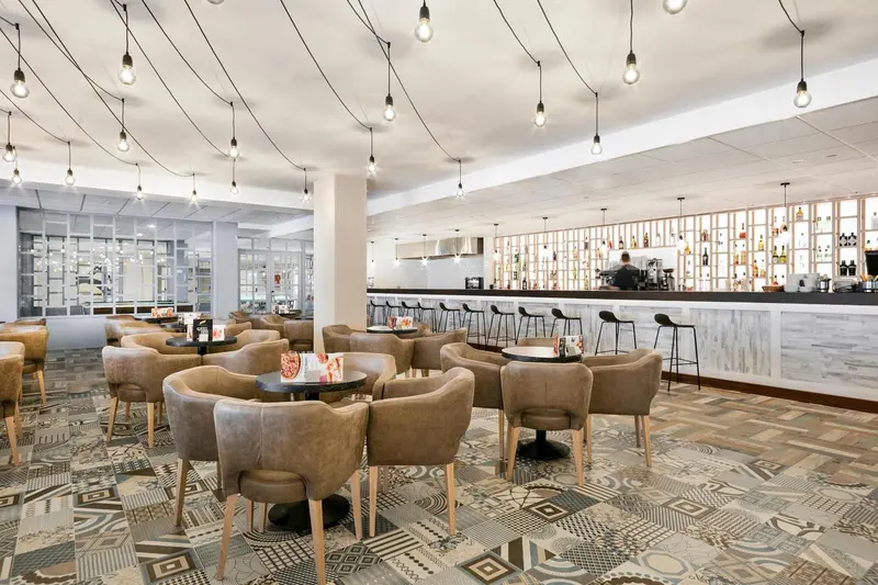 Une salle lumineuse avec des tables et des chaises, un long comptoir et des suspensions décoratives.