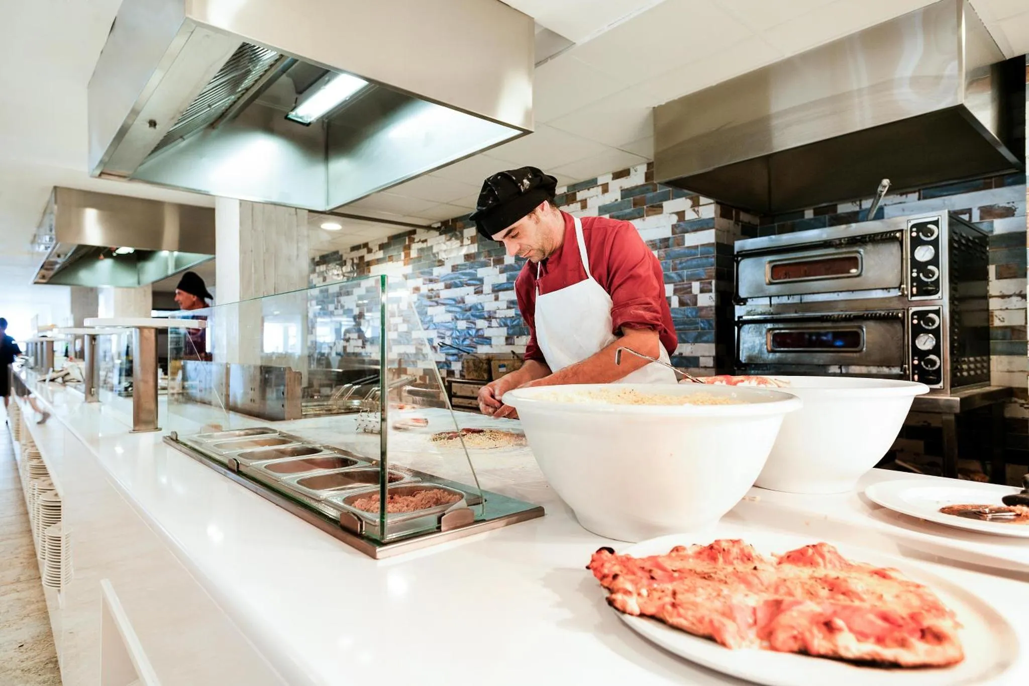 Un chef prépare des pizzas devant un comptoir de buffet.