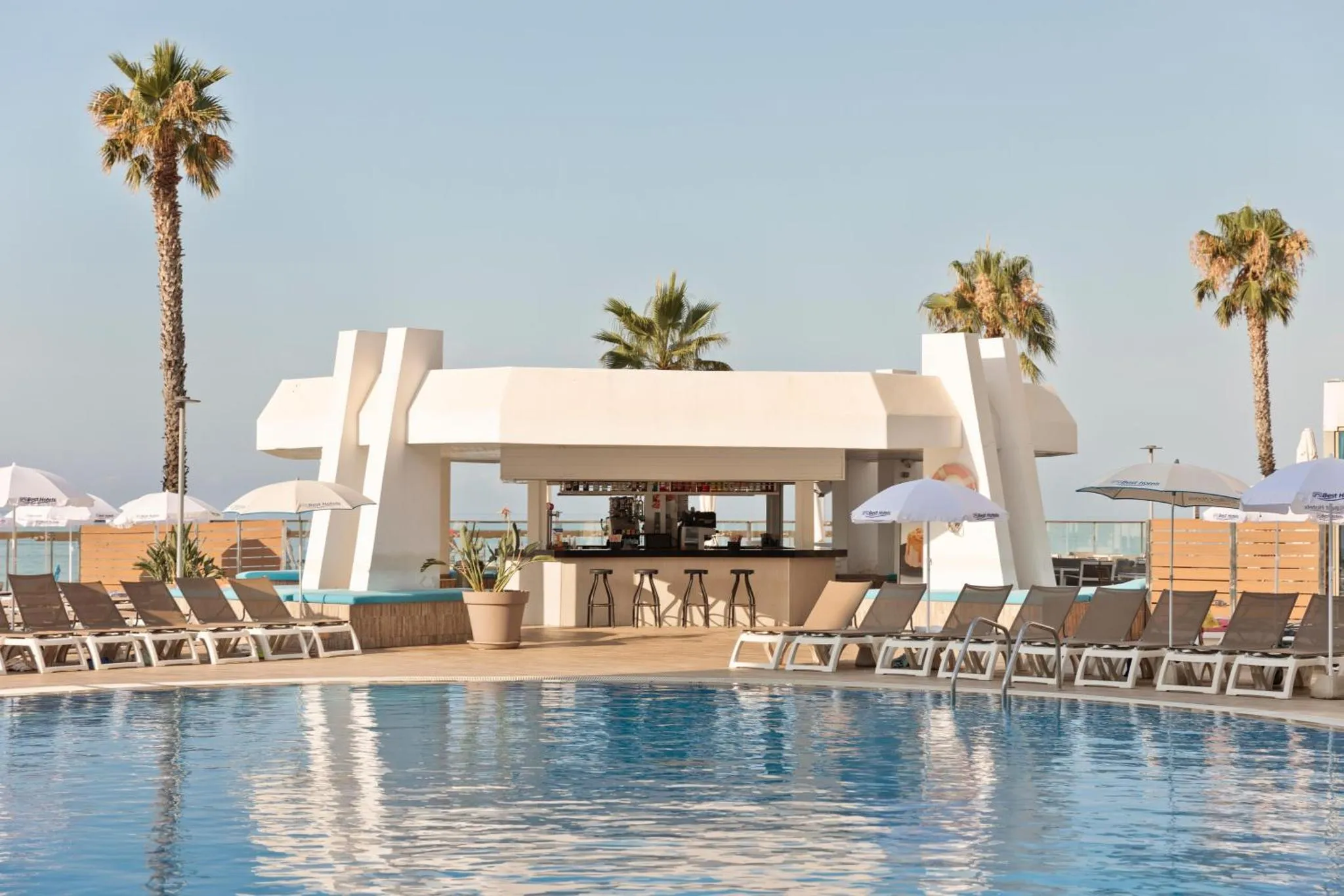 Terrasse avec bar et transats au bord d'une piscine ensoleillée.