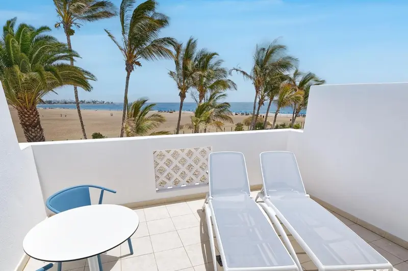 Terrasse avec mobilier blanc donnant sur une plage de sable.