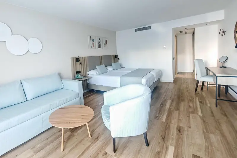 Espace de vie lumineux avec canapé, fauteuil et lit double.