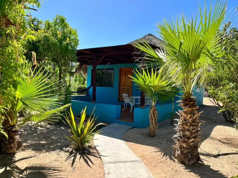 Une petite maison turquoise avec une porte en bois et une terrasse ombragée.