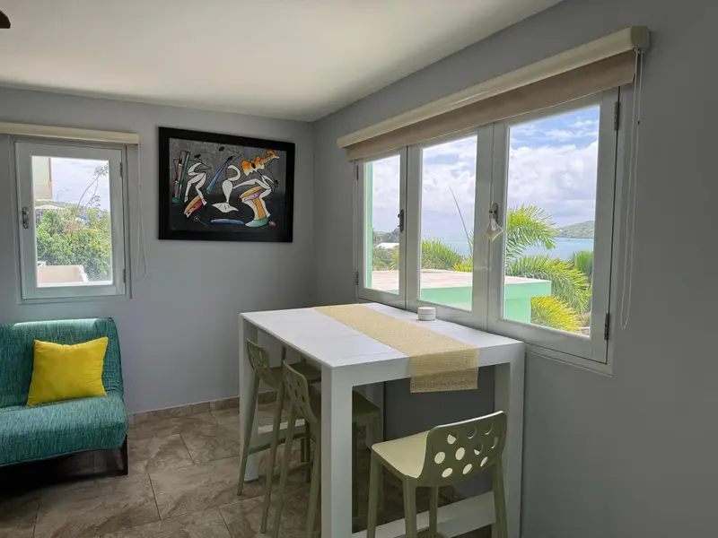 Une table à manger est placée devant de grandes fenêtres ouvertes sur un paysage tropical.