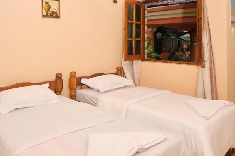Une chambre lumineuse avec deux lits simples et une fenêtre ouverte.
