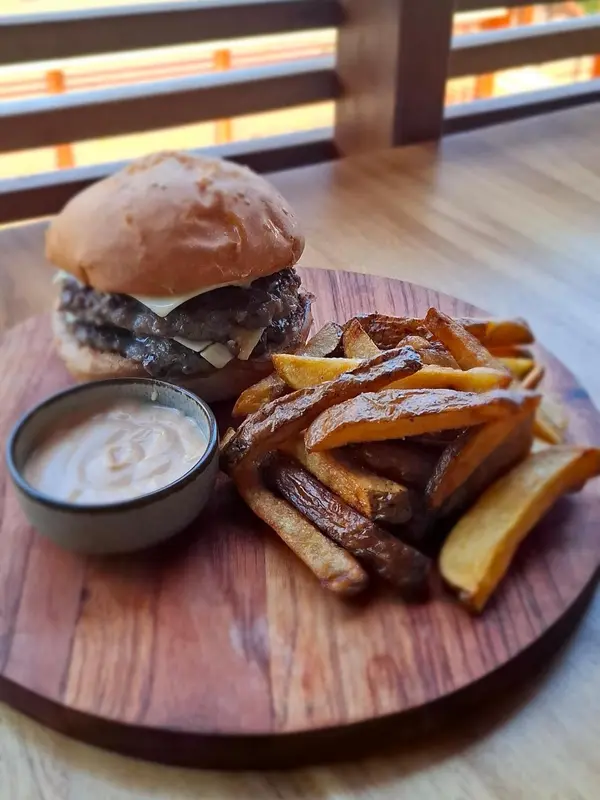 Un hamburger avec des frites et une sauce est présenté sur une planche en bois.