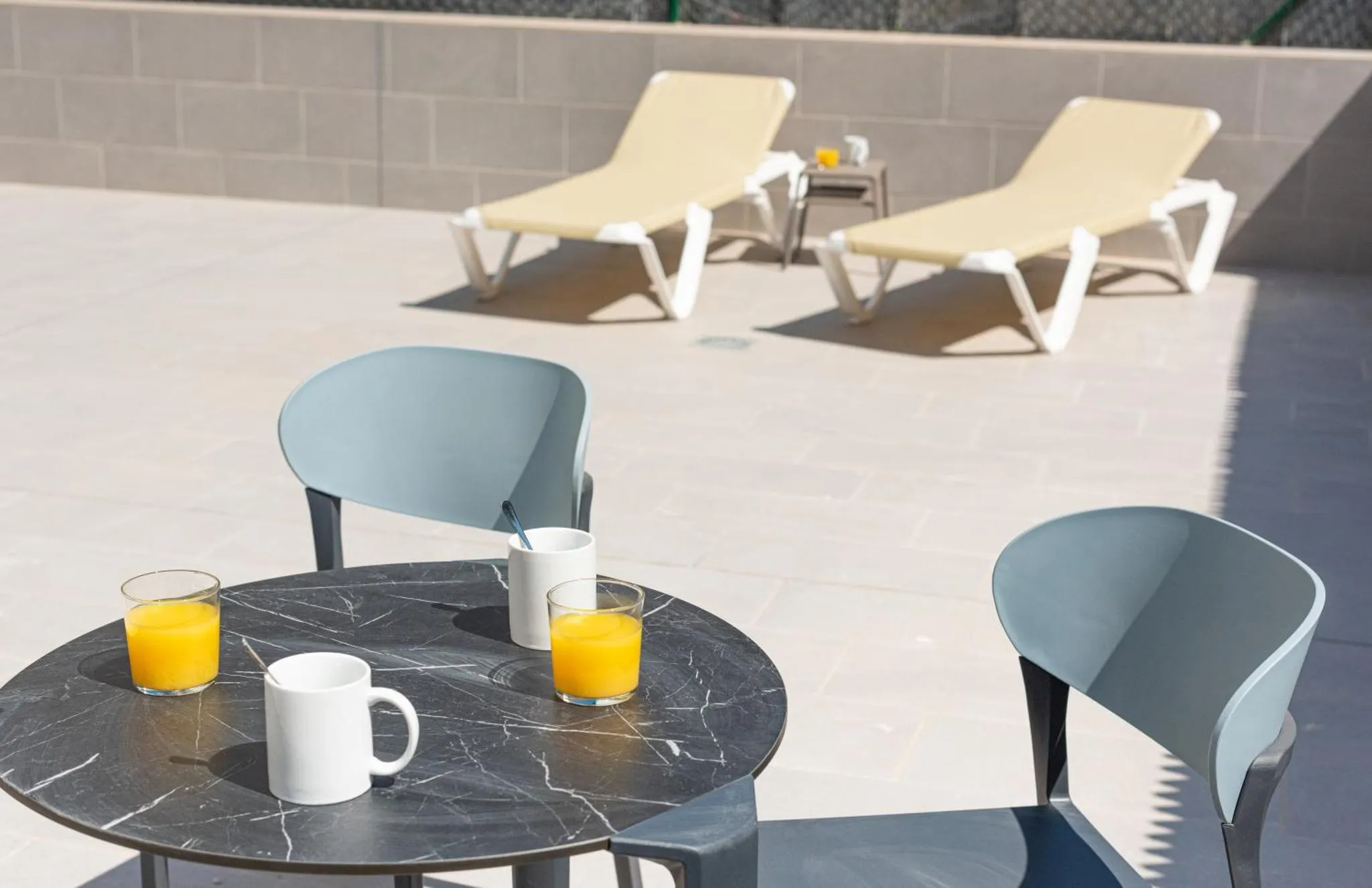 Deux transats et tables basses avec boissons sur une terrasse ensoleillée.