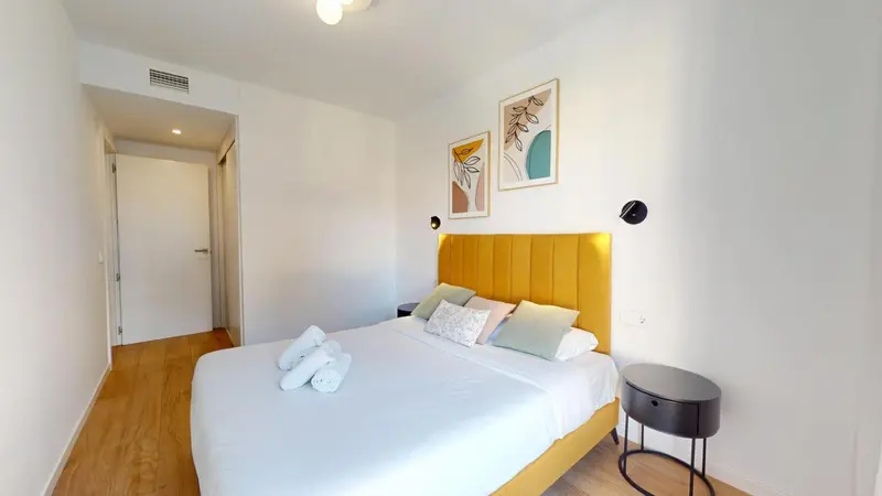 Une chambre lumineuse avec un grand lit recouvert d'une courtepointe blanche et de coussins.
