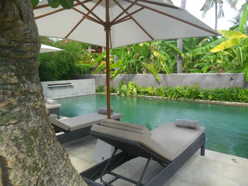Transats et parasols bordent une piscine turquoise dans un jardin tropical.