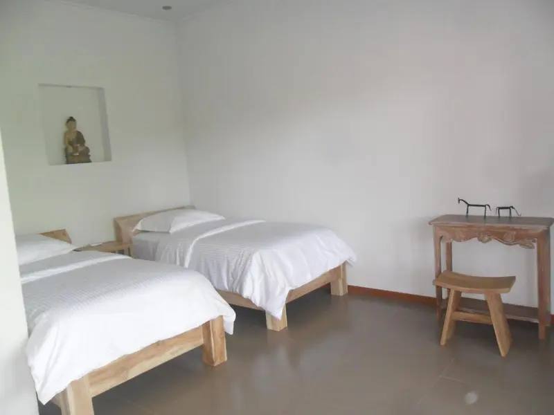 Une chambre lumineuse avec deux lits simples et une petite table en bois.