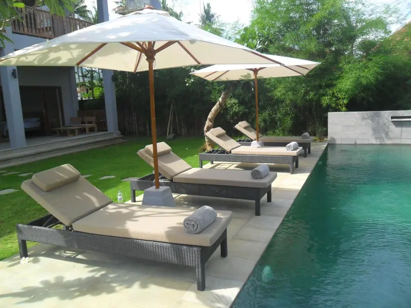 Transats et parasols bordent une piscine turquoise dans un jardin soigné.