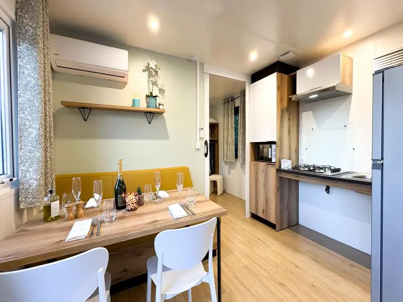 Une table est dressée dans une pièce lumineuse avec une cuisine équipée en fond.