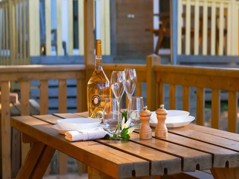 Une table en bois est dressée pour un repas en extérieur avec de la vaisselle et des bouteilles.