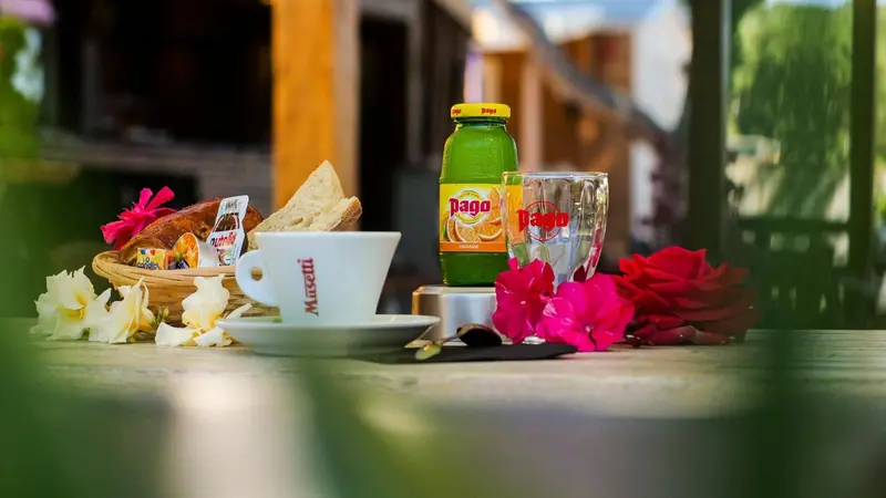 Une table en bois présente un petit-déjeuner avec des viennoiseries, une boisson et des fleurs.