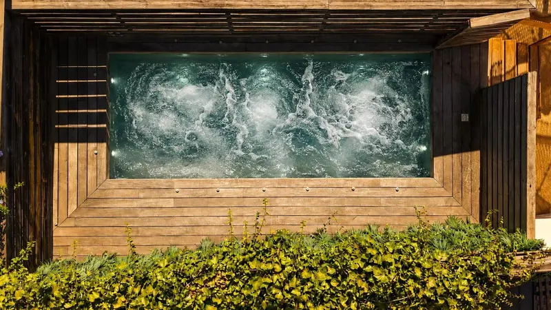 Vue aérienne d'une piscine rectangulaire turquoise entourée de bois et de végétation.