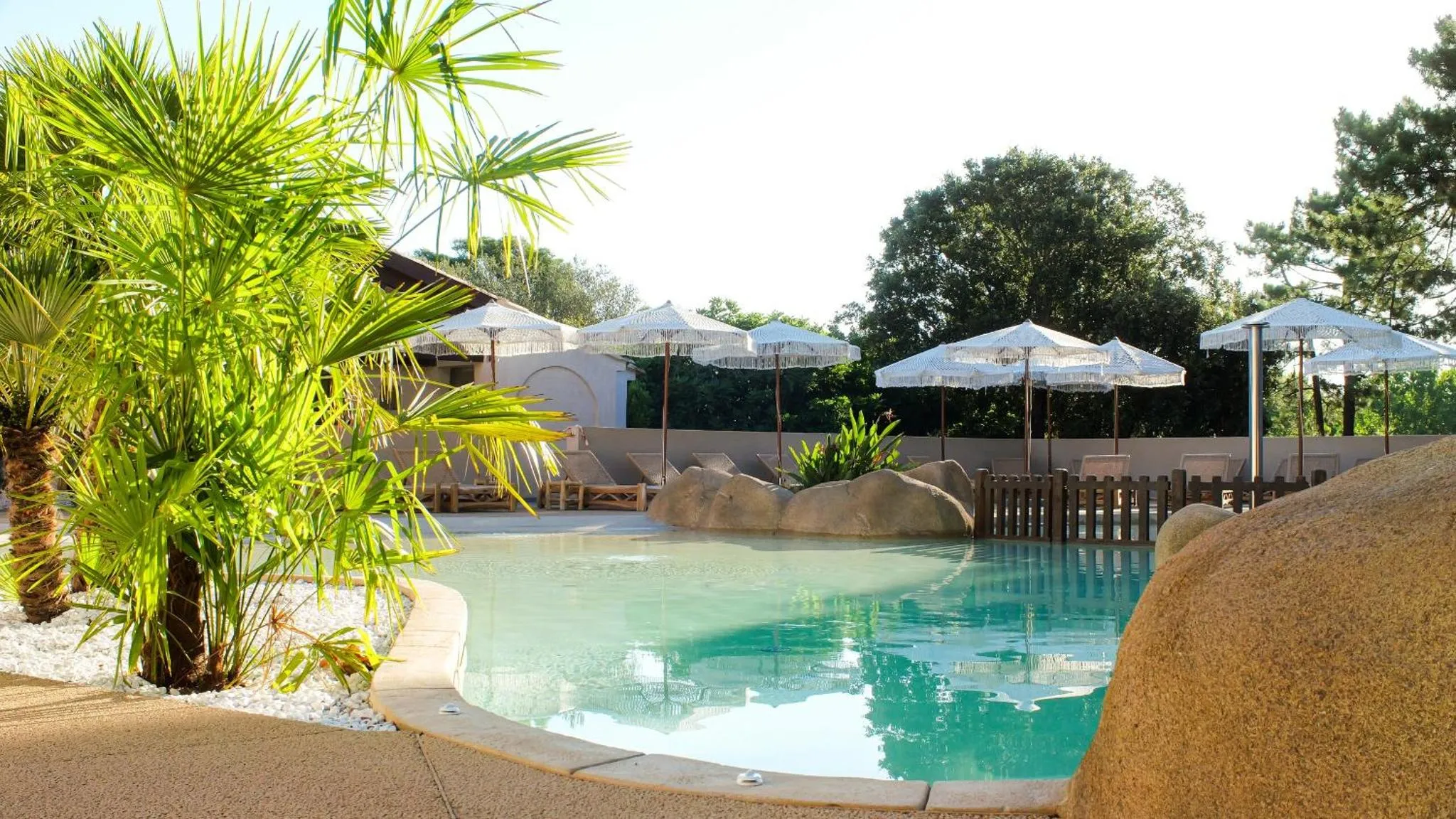 Une piscine bordée de rochers et de végétation tropicale, avec des transats et des parasols.