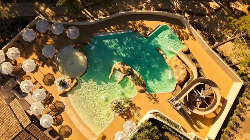 Vue aérienne d'une piscine aux formes organiques entourée de transats sous des parasols.