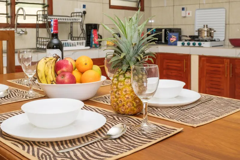 Une table en bois est dressée avec de la vaisselle, des fruits frais et une bouteille de vin.