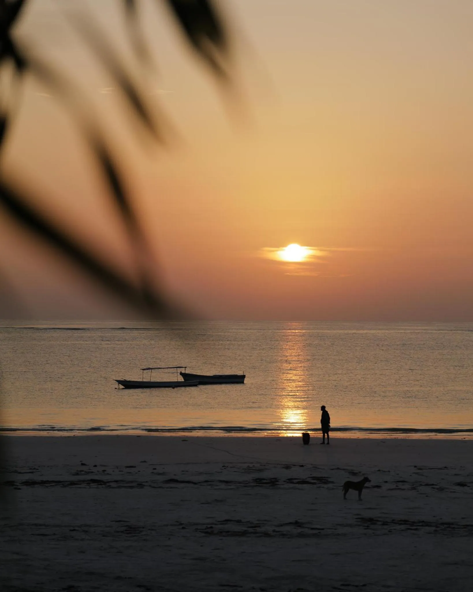 Coucher de soleil sur une plage avec un bateau et des personnes au loin.