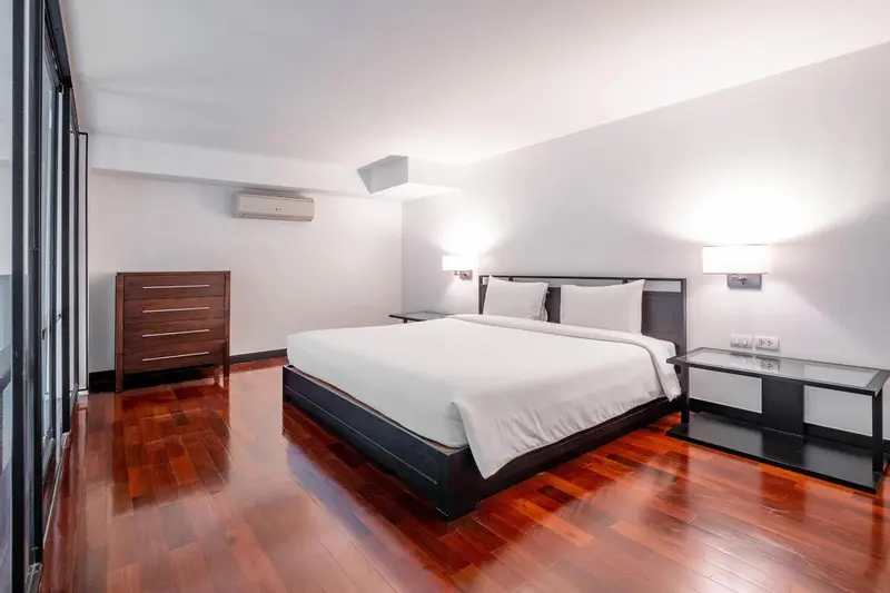 Une chambre lumineuse avec un grand lit et un parquet en bois.