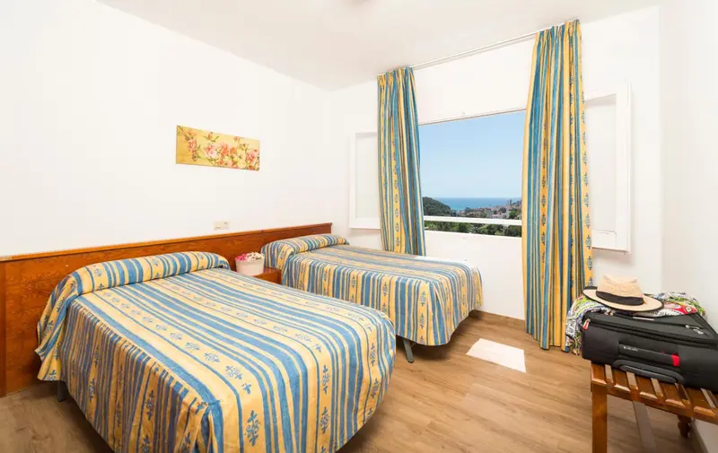 Chambre lumineuse avec deux lits et vue sur la mer.