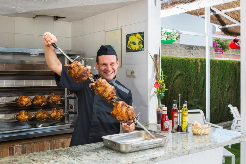 Un homme souriant présente des poulets rôtis devant un four.