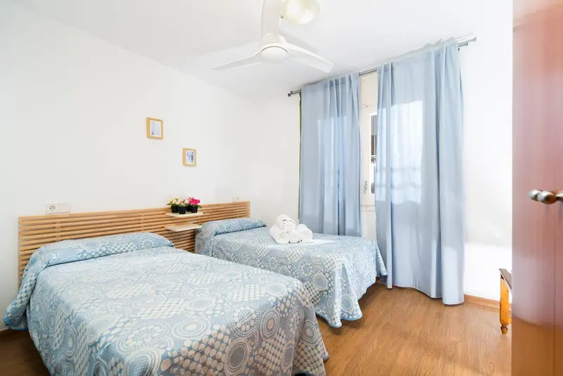 Chambre lumineuse avec deux lits simples et rideaux bleus.