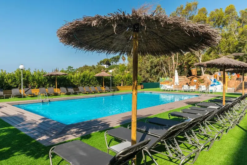 Transats noirs disposés autour d'une piscine rectangulaire sous des parasols en chaume.