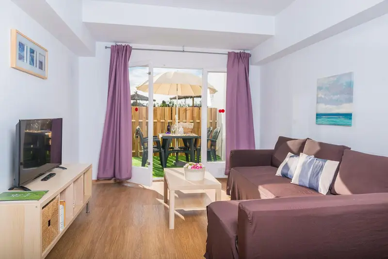 Un salon lumineux avec canapé et télévision donnant sur une terrasse.