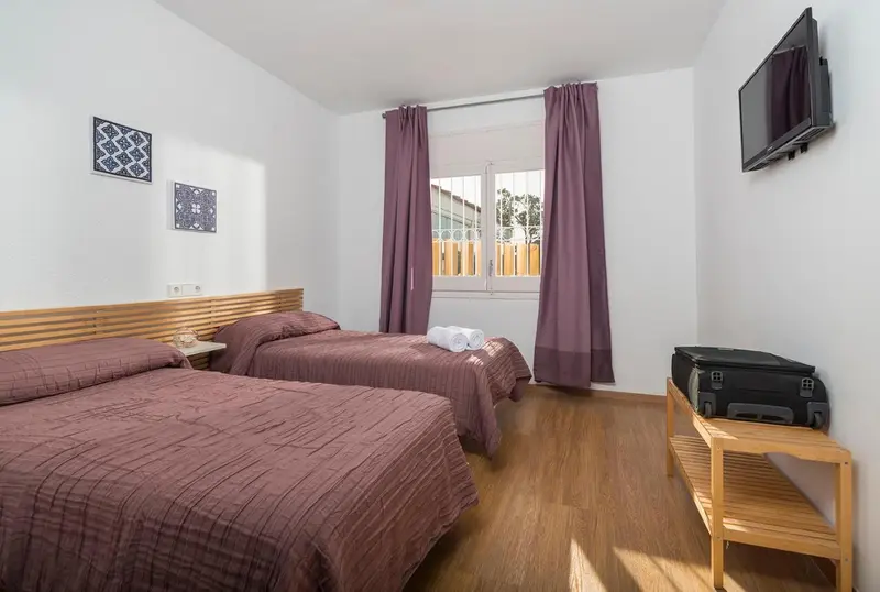 Une chambre lumineuse avec deux lits simples et une télévision murale.
