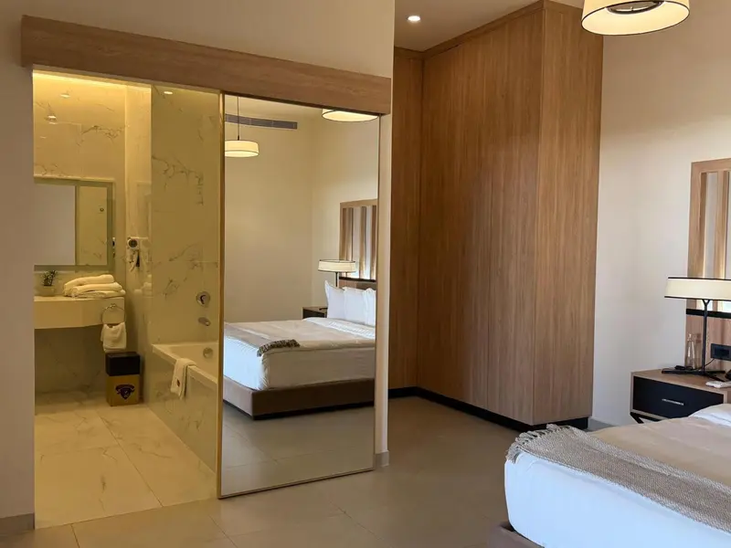 Une chambre lumineuse avec un lit et un espace baignoire visible à travers une cloison vitrée.