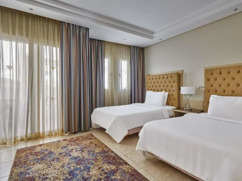 Une chambre lumineuse avec deux lits simples et un tapis décoratif.