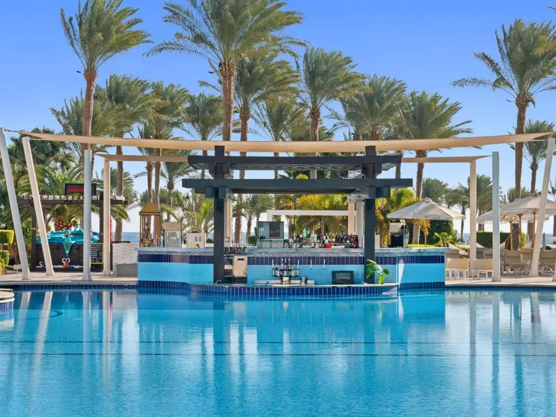 Une piscine turquoise bordée de chaises longues et d'un bar extérieur.