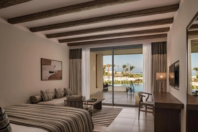 Une chambre lumineuse s'ouvre sur une terrasse avec vue sur la piscine et la mer.