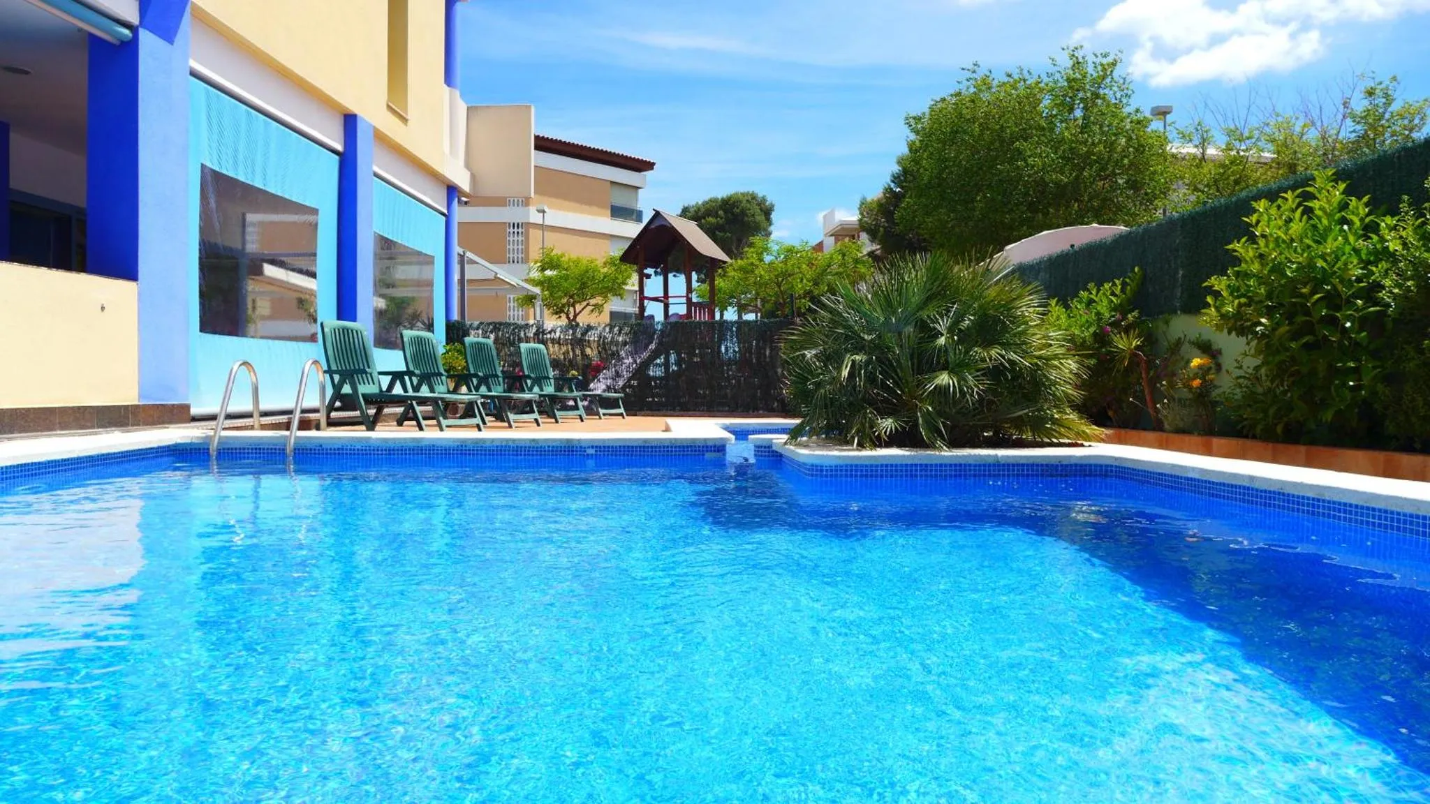 Une piscine rectangulaire avec des transats verts et une végétation luxuriante.