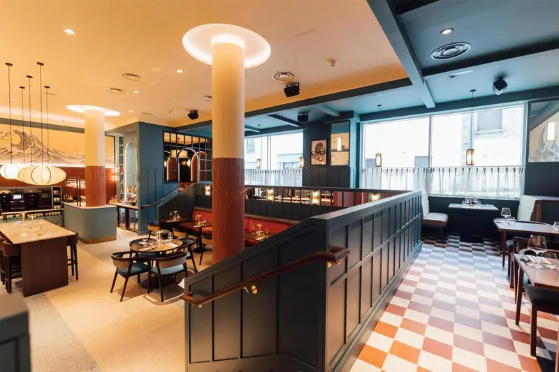 Une salle de restaurant lumineuse avec des tables dressées et un comptoir de bar.