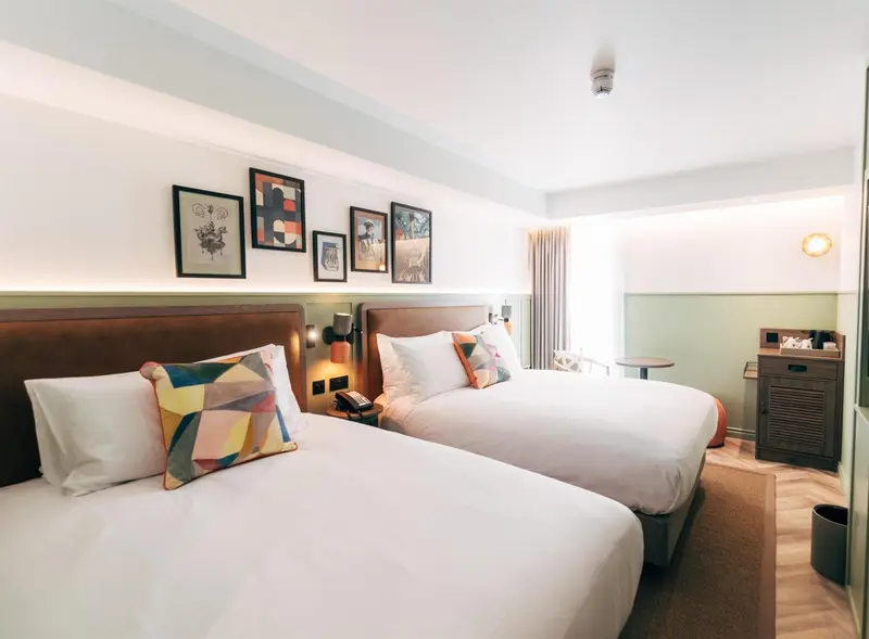 Une chambre lumineuse avec deux lits simples et une décoration murale.