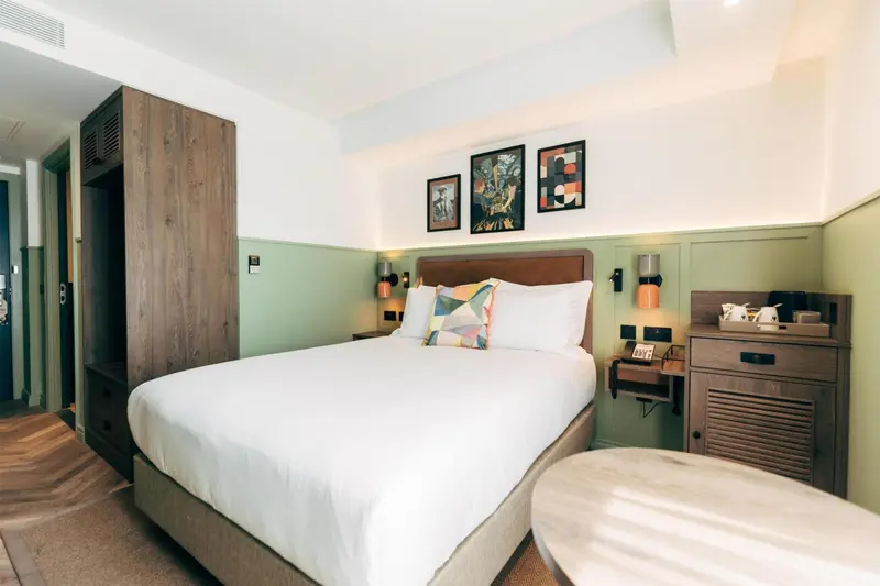 Une chambre lumineuse avec un grand lit recouvert d'une couette blanche et de coussins colorés.