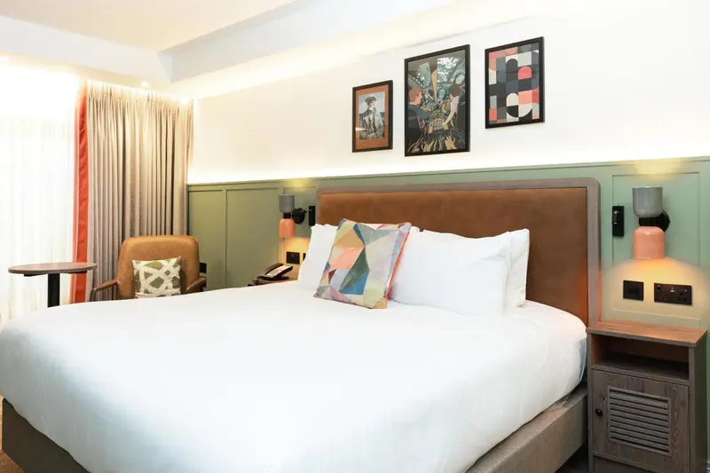 Une chambre lumineuse avec un grand lit recouvert d'une couette blanche et de coussins colorés.