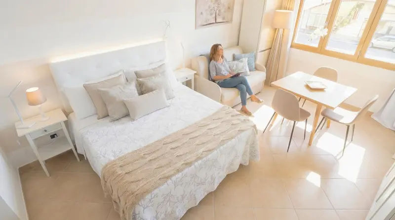 Une femme est assise sur un canapé dans un espace de vie lumineux avec un lit et une table.