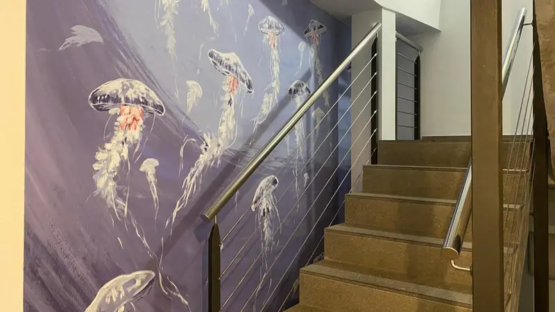 Un escalier beige avec une rampe en métal mène à un mur décoré de méduses.