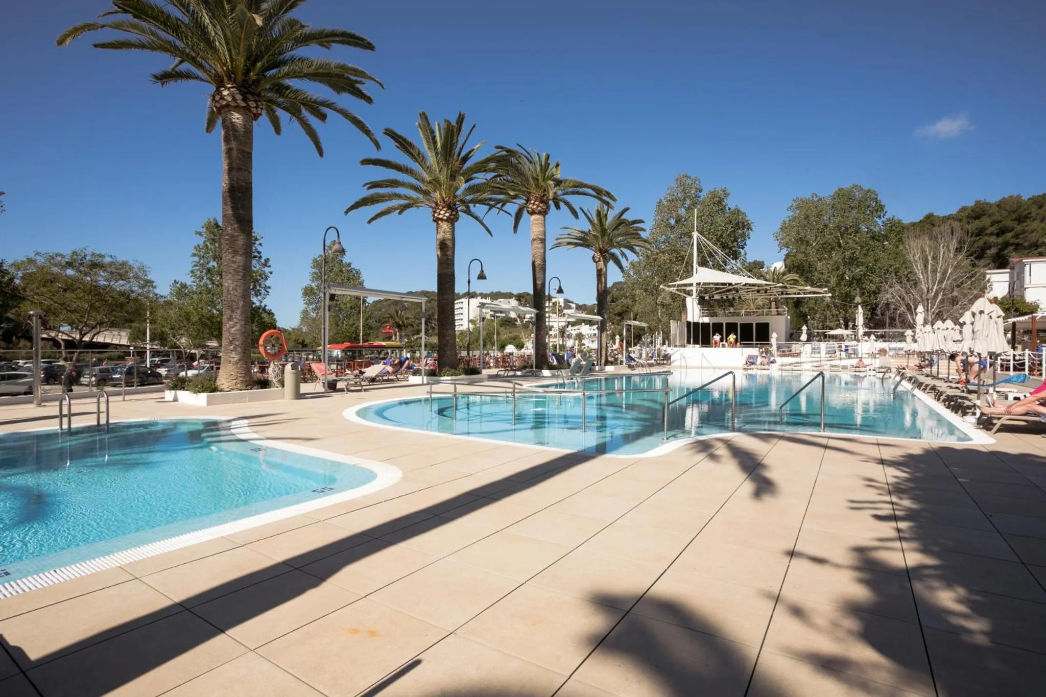 Piscines ensoleillées entourées d'un espace aménagé avec des transats et des palmiers.
