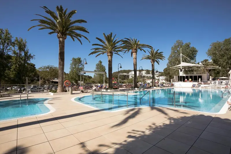 Piscine extérieure avec transats et palmiers sous un ciel bleu.