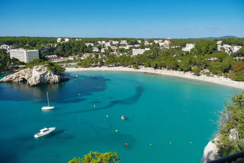 Vue aérienne d'une crique turquoise bordée d'une plage de sable fin et de bâtiments.