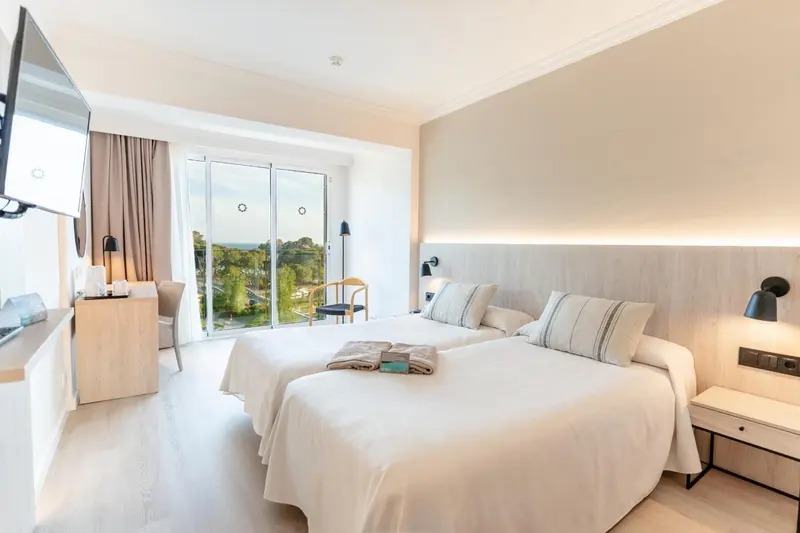 Chambre lumineuse avec deux lits simples et vue sur la végétation.