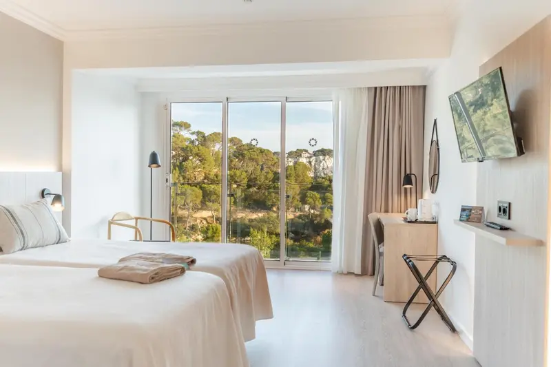 Chambre lumineuse avec deux lits simples et vue sur la végétation.