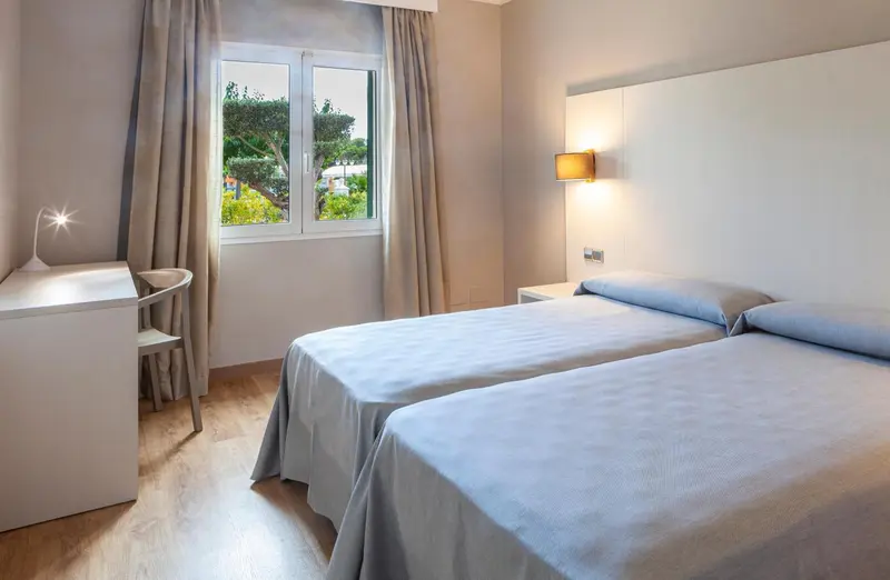Une chambre lumineuse avec deux lits simples et un bureau près de la fenêtre.