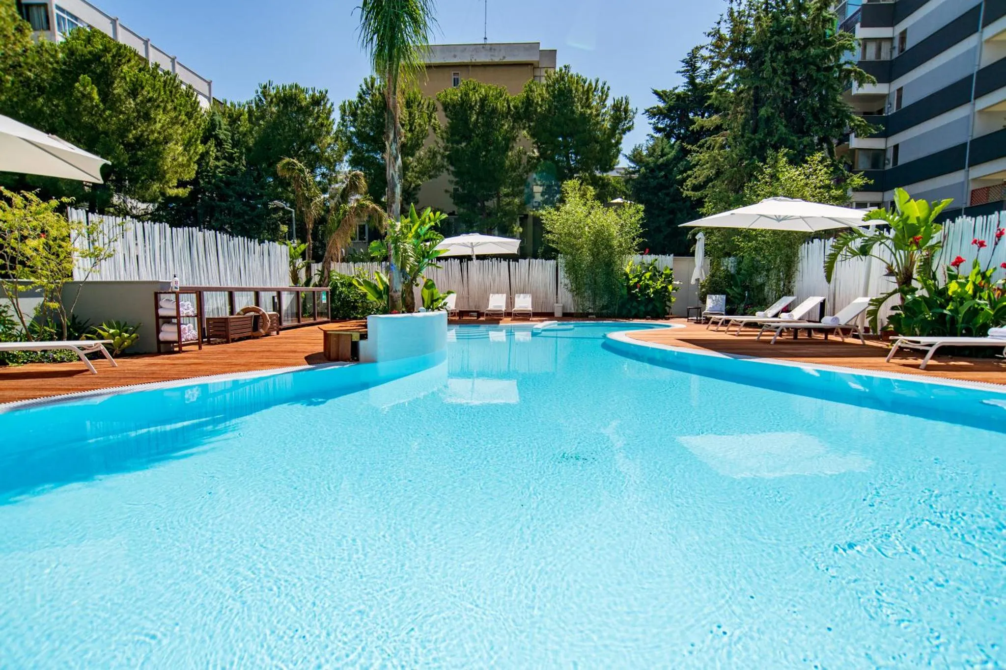 Une piscine turquoise bordée de transats blancs sous des parasols.